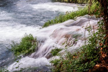Krka Ulusal Parkı 'ndaki küçük şelalelerden dökülen sular, bereketli bitki örtüsü ve canlı yeşilliklerle çevrili ve Hırvatistan' ın açık hava güzelliğini somutlaştıran çarpıcı bir doğal manzara yaratıyor.