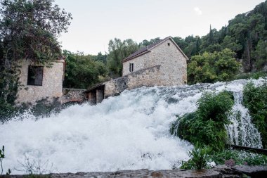 Hırvatistan 'ın Krka milli parkındaki eski bir taş değirmeni etrafındaki kayaların üzerine dökülen beyaz su, doğa ve tarihin pitoresk bir manzarasını yaratıyor.