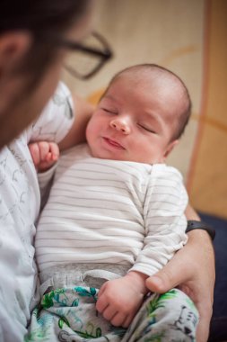 Huzurlu yeni doğmuş bebek bir ebeveynin rahatlatıcı kucaklamasında mışıl mışıl uyuyor. Şefkatli an, ebeveyn sevgisinin özünü ve çocukluğun sükunetini yakalar.