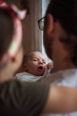 Sevimli yeni doğan bebek, ebeveynlerinin sevgi dolu kucaklamalarında uzanırken esniyor ve geriniyor. Erken yaşta ebeveynlik sırasındaki sıcaklık ve bağlarla dolu hassas bir anı yakalıyor.