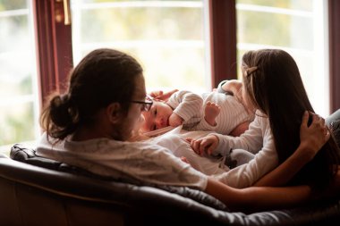 Genç bir aile evdeki rahat bir kanepede dinleniyor, yeni doğmuş bebekleri ve küçük kızlarıyla bağ kuruyor, birlikte huzurlu bir anın ve sevginin tadını çıkarıyorlar.