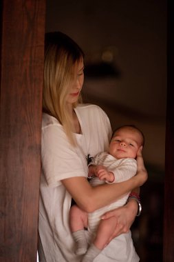 Anne kucağında küçük oğlunu kucaklar sevgi ve bağla dolu hassas bir anı somutlaştırır. Evlerinin sıcak atmosferiyle çevrelenir.