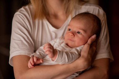Genç anne, yeni doğmuş bebeğini kollarında kucaklıyor, sevgi ve şefkat yayıyor. Sıcak, samimi bir an boyunca. Bağlantı ve neşeyle dolu.