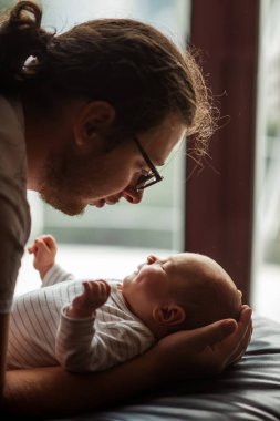 Baba sevgiyle kollarında beşikteki yeni doğan bebeğine bakıyor. Samimi sahne, ebeveyn ve çocuk arasındaki bağı vurgulayan derin bir bağ ve sıcaklık yakalar.