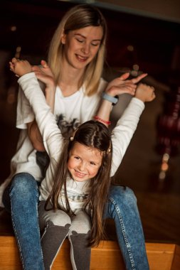 Neşeli anne ve kızı birlikte evde güzel vakit geçiriyorlar. Çocuk annesinin kucağında mutlu bir şekilde oturuyor, her ikisi de sıcak bir ortamda kahkaha ve iletişim anlarını paylaşıyor.