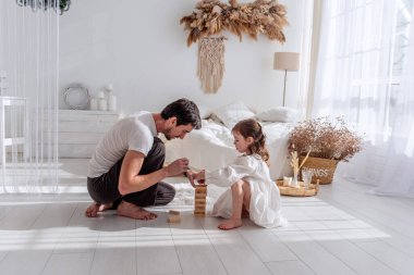 Baba ve kızı birlikte güzel vakit geçiriyorlar, parlak ışıklı bir yatak odasında ahşap bloklardan bir kule inşa ediyorlar, sıcak ve sevgi dolu bir aile anı yaratıyorlar.