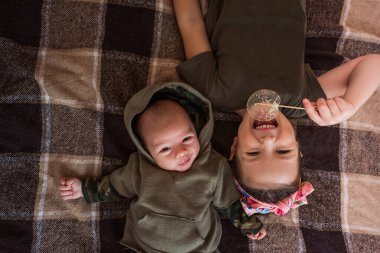 Ablam kareli bir battaniyeye baş aşağı uzanmış, yeni doğan erkek kardeşiyle yakınlaşırken tatlı bir izomalt lolipopun tadını çıkarıyor, sıcak bir aile sevgisi ve sevgi anı yaratıyor.