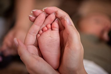 Annenin elleri yeni doğmuş bebeğinin küçük ayaklarını nazikçe kucaklıyor sevgi, şefkat ve ebeveynliğin güzel bağıyla dolu kalpten bir anı yakalıyor.