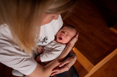Genç anne, evde sessiz bir süre boyunca esneyen bebeğini kollarında tutuyor. Doğal ışıklandırma, bebek yorgunluk belirtileri gösterirken, özel bir atmosfer yaratır.