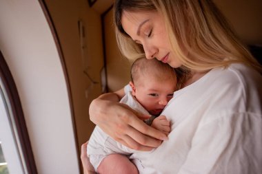 Huzurlu bir anne, yeni doğmuş bebeğini nazikçe bir pencerenin kenarında tutarak erken anneliğin sıcaklığını ve bağını yakalar. Yumuşak ışık onların barışçıl bağlantılarını vurgular