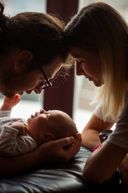 Ebeveynler yeni doğan bebeklerini sevgiyle kucaklayarak sıcak ve samimi bir aile bağı kurarken şefkatli bir an. Yumuşak ışık, duygusal bağlantıyı ve besleyici atmosferi vurgular