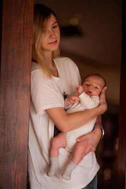 Genç anne yeni doğmuş bebeğini sıcak, rahat bir yuva ortamında nazikçe kucaklıyor. Samimi an, anne ve çocuk arasındaki bağ ve şefkati yakalar, erken ebeveynliğin altını çizer.