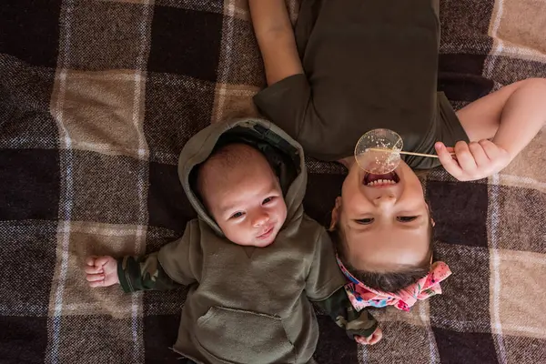 Ablam kareli bir battaniyeye baş aşağı uzanmış, yeni doğan erkek kardeşiyle yakınlaşırken tatlı bir izomalt lolipopun tadını çıkarıyor, sıcak bir aile sevgisi ve sevgi anı yaratıyor.