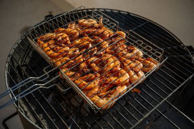 Taze karidesler ızgarada ızgara yapıyor. Közlerin içine düşmesini önlemek için metal bir ızgara kullanıyorlar. Lezzetli ve dumanlı bir deniz mahsulü yemeği yapıyorlar.