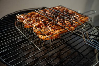Taze karidesler, sıcak kömürlerin üstünde ızgara yapıyor. Açık hava yemek pişirme deneyimi sırasında havayı dolduran enfes ve dumanlı bir koku yaratıyorlar.