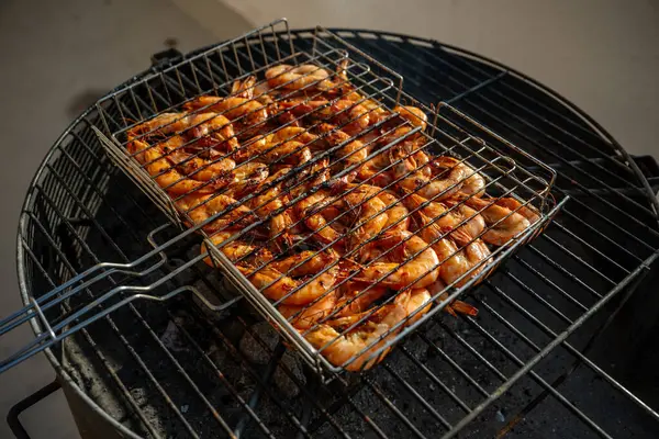 Taze karidesler ızgarada ızgara yapıyor. Közlerin içine düşmesini önlemek için metal bir ızgara kullanıyorlar. Lezzetli ve dumanlı bir deniz mahsulü yemeği yapıyorlar.