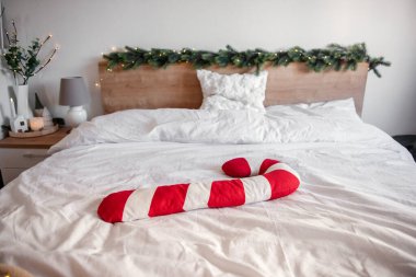 Büyük kırmızı ve beyaz noel şekerleme yastığı süslü bir yatak odasındaki yapılı bir yatakta dinleniyor. Bu da hoş ve şenlikli bir atmosferi işaret ediyor.
