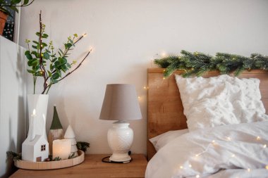 Konforlu bir yatak odasını ahşap mobilyalar, beyaz bir lamba, mumlar, cüceler ve köknar dallarıyla aydınlatan Noel ışıkları sıcak ve şenlikli bir atmosfer yaratıyor. Şenlikli iç mekan 