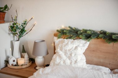 Noel ışıkları köknar dallarını aydınlatıyor ve ahşap komodinin ve yatak başlığının üzerine dekoratif eşyalar yerleştiriyor, kış tatillerinde yatak odasında rahat bir atmosfer yaratıyor.