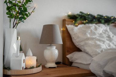 Noel süslemeleri mumlar, dekoratif evler ve peri ışıkları aydınlatan yatak odası, rahat yatağın yanında rahat bir kış ortamı yaratmak