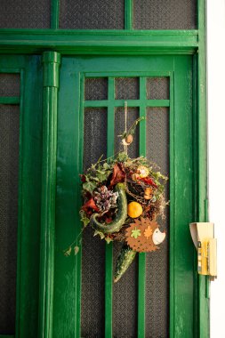 Süslü bir sonbahar çelengi içeren yeşil ahşap giriş kapısı, kabak, kurumuş yapraklar, dallar, böğürtlenler ve güz mevsimini kutlayan sevimli bir kirpi figürü.