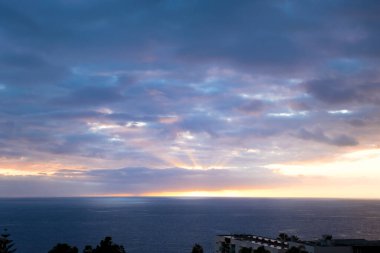 Güneş ışınları gün batımında bulutların arasından geçer. Portekiz, Madeira Adası Funchal 'da parlak renkli bir akşam.