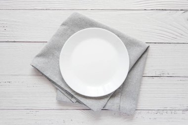 Empty white plate on grey napkin, top view, minimalist style composition on white wooden table, for menu or dish presentation.