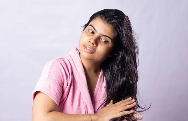A beautiful Indian woman applying hair oil on her black hair with smile on white background