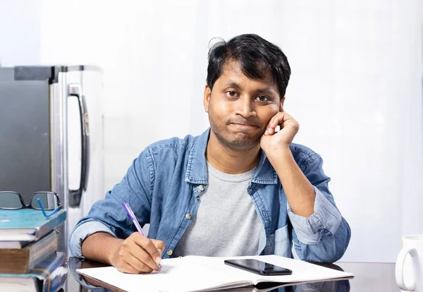 An Indian young male looking worried and thinking while studying at home on white background