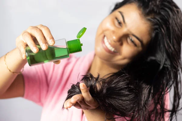 Selective focus on hair oil being applied by a beautiful indian woman with smile on white background