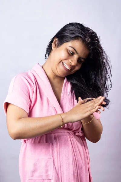 A beautiful Indian woman applying hair oil on her black hair with smile on white background