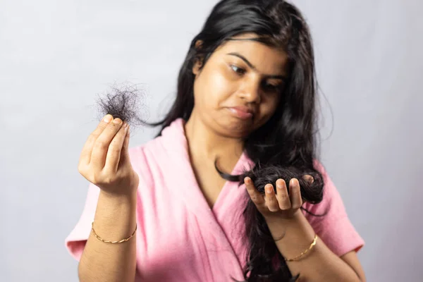 Selective focus on fallen hair held in hand by a worried Indian woman on white background