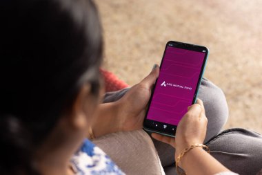 Birbhum, West Bengal, India - December 27th 2022: An Indian woman with smart phone using Axis mutual fund application at home