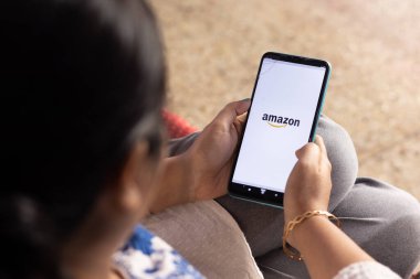 Birbhum, West Bengal, India - December 27th 2022: An Indian woman with smart phone looking at Amazon online shopping site at home