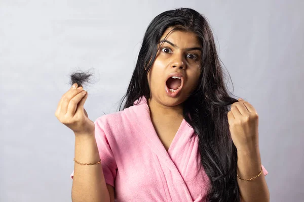 A worried Indian girl in pink bathrobe with hair fall problem on white background