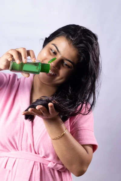 Selective focus on hair oil being applied by a beautiful indian woman with smile on white background