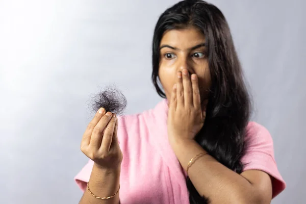 Selective focus on fallen hair held in hand by a worried Indian woman on white background