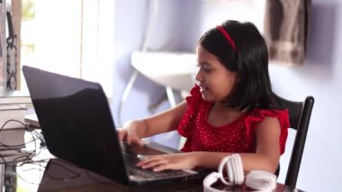 Kırmızı elbiseli şirin bir Hintli kız evde dizüstü bilgisayarla ders çalışıyor.