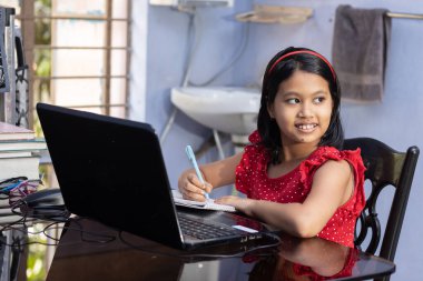 Kırmızı elbiseli şirin bir Hintli kız evde dizüstü bilgisayarla ders çalışıyor.