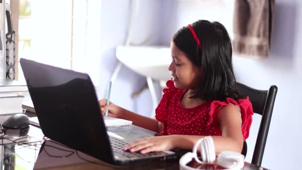 インドのかわいいです女の子子供で赤ドレスで家で勉強とともにラップトップ — ストック動画