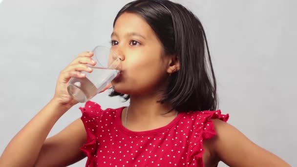 白い背景のガラスから水を飲む赤いドレスのインド人の女の子 — ストック動画