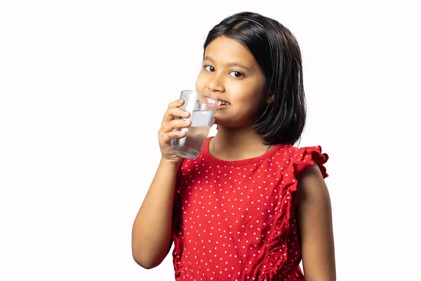 stock image An Indian asian girl child in red dress drinking water from a glass on white background