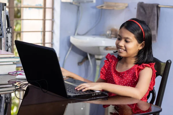 Kırmızı elbiseli şirin bir Hintli kız evde dizüstü bilgisayarla ders çalışıyor.