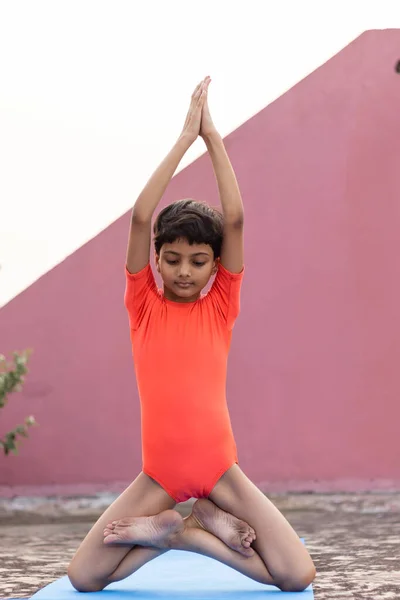 Hintli bir kız çocuğu yoga minderinde parbatasana yogası yapıyor.