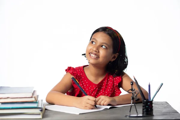 かなり美しいですインドの女の子勉強と上を見上げます勉強テーブルとともに本上に白い背景 — ストック写真