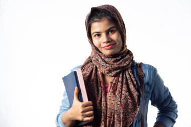 Elinde kitaplarla beyaz arka planda gülümseyen bir Hintli genç Müslüman kız.