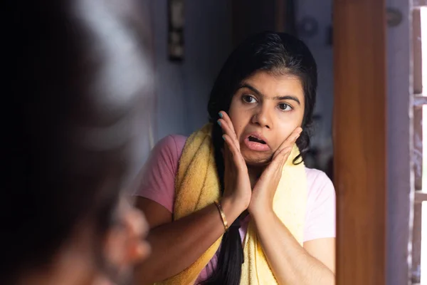 An Indian woman female girl in front of mirror looking at her skin with worried face