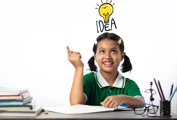 白い背景にアイデア電球の記号を上を向いて笑顔で研究テーブルで勉強かなり美しいですインドの女の子 — ストック写真