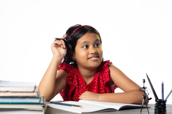 美しいインドの少女の子供が白い背景の本と勉強テーブルで上向きに考えている — ストック写真