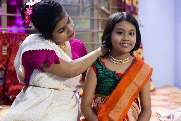An Indian mother helping her girl child to wear traditional ornaments indoors at a festival night